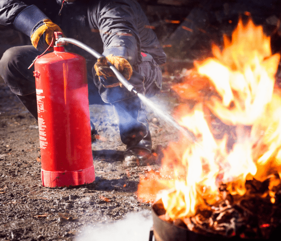 Basic Fire Training Perth Demonstrate First Attack Firefighting Equipment - Man in fire safety clothing extinguishing a large fire with a red fire extinguisher in a burnt area.