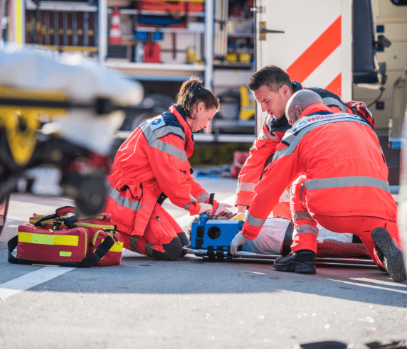 Three people preforming onsite First Aid to a person laying on the ground in a restraint position.