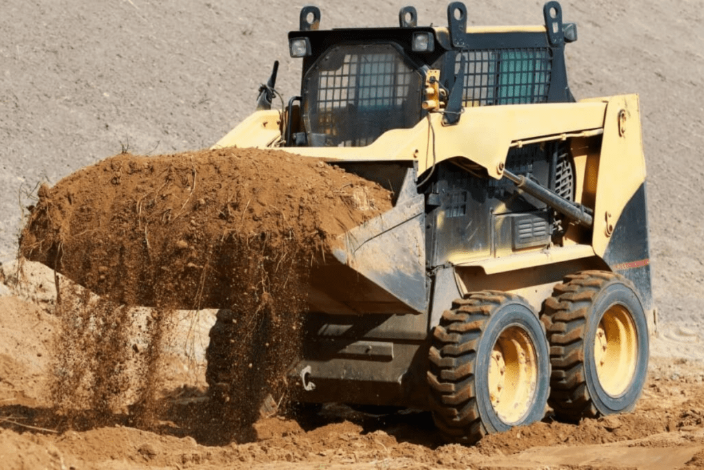 Skid Steer being operated on by Skid Steer driver lifting a bucket full of dirt at a jobsite.
