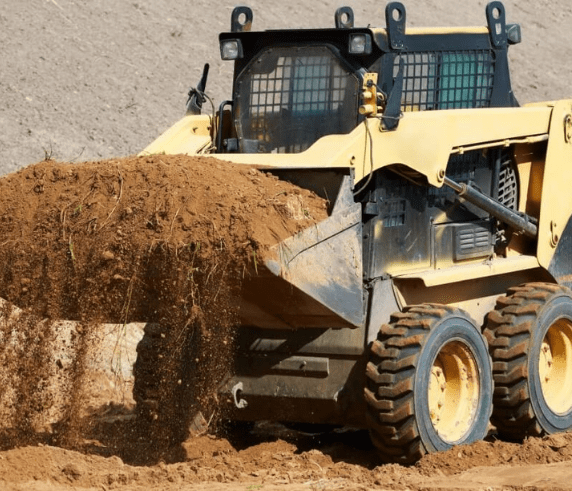 Skid Steer being operated on by Skid Steer driver lifting a bucket full of dirt at a jobsite.