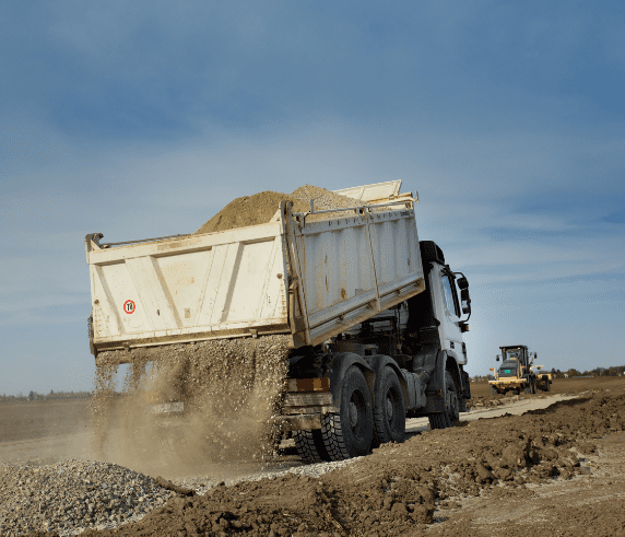 Conduct Tip Truck Operations. Tip truck unloading soil on a large construction site.