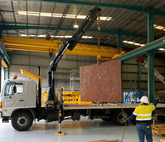 Vehicle Loading Crane Licence Perth - Participant Operating Crane. A vehicle loading crane lifting a large slab onto a truck in an industrial warehouse