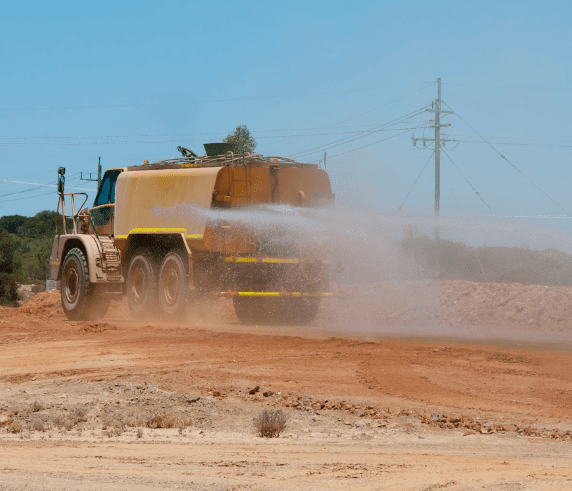 Conduct Water Vehicle Operations. A water truck spraying to control dust on a dry and dusty construction site.