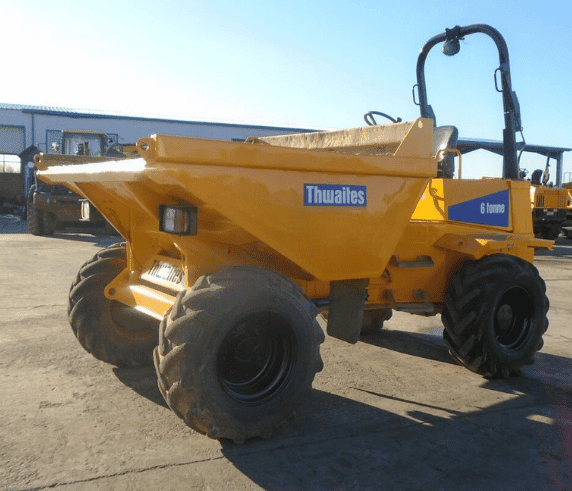 Conduct Articulated Dump Truck Operations. Bright yellow Thwaites 6-tonne articulated dump truck on an industrial yard with construction equipment in the background