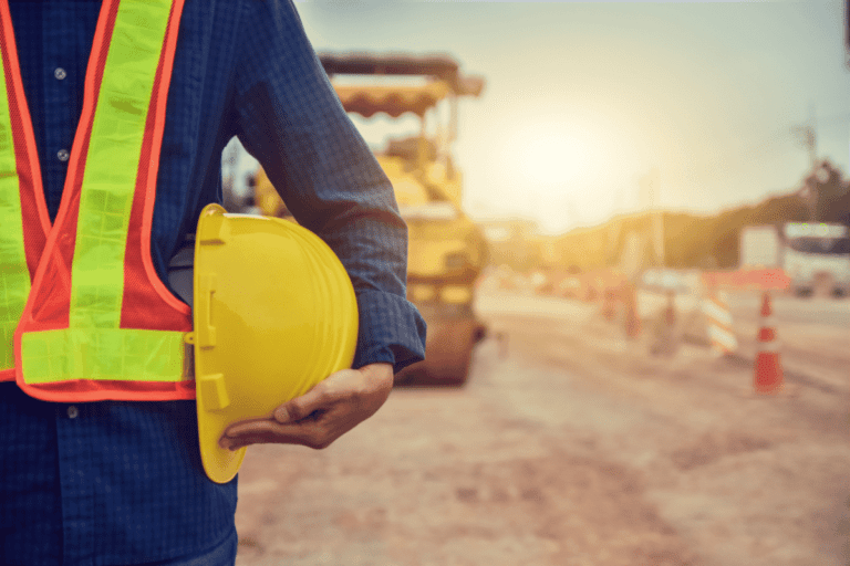 Man holding a yellow hardhat helmet under his arm with a roller machine in the background.